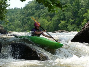 a girls camp camper paddles a green kayak over a rapid
