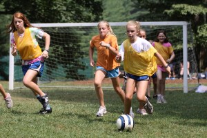 Girl at camp dribbles past defender with soccer ball