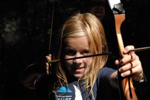 girl holds back arrow in archery at camp