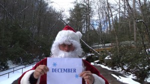Santa holds sign for December at Sliding Rock.