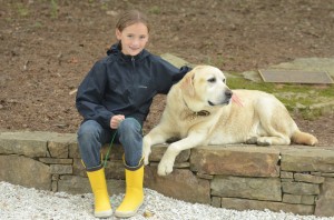 A camper with yellow boots poses with Newton, the Summer Camp Dog.