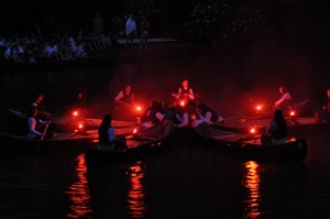 Summer camp canoes in formation with flares lighted.