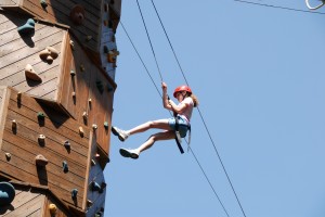 Summer camp girl learns to rappel on the climbing tower at Camp Illahee.