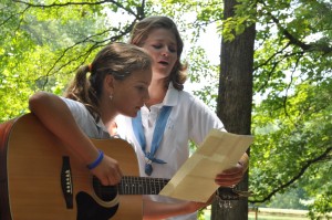 A summer camper plays guitar while her counselor sings.