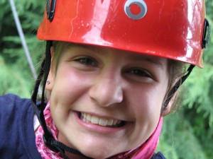 A summer camp girl smiles in a climbing helmet.