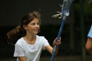 Summer camp girl with lacrosse stick throws the ball.