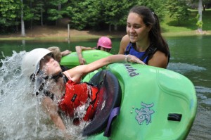 A summer camp counselor helps a girl learn to roll a kayak.