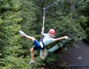 Illahee summer camp girl rides the zipline with arms outstretched.