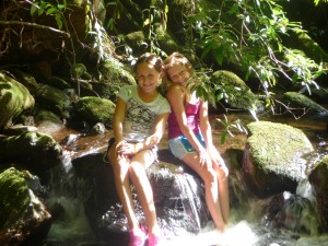 Two girls campers sitting on a mini waterfall.