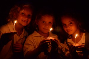 Three young girls camp campers with candles on the final night of camp.