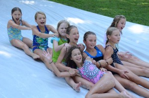 A bunch of giggling summer camp girls sliding down the Slip n Slide at Camp Illahee.