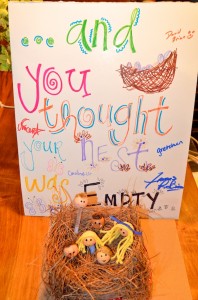 A nest filled with dolls representing the Illahee crew sits beneath a sign that says "and you thought your nest was empty."