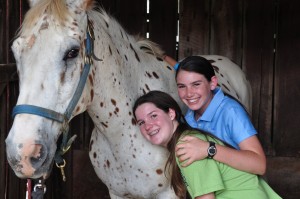 Two Camp Illahee campers hug a dappled horse.