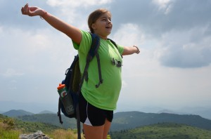 Camper spreads arms with mountain vistas in background.