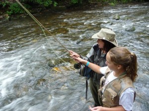 A camper holds a flyrod with the assistance of her instructor.