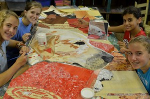 Summer camp counselors and campers work on a joint "paper painting" project.