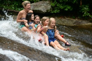 A summer camp counselor slides down Sliding Rock with her campers at Camp Illahee.
