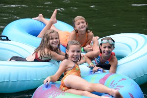 Four summer campers lounging in the Camp Illahee swim lake on blue inner tubes.