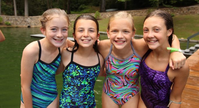 Four campers arm and arm swim in the swim lake.