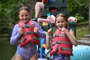 Two Illahee campers in bathing suits and life jackets give the thumbs up before jumping in the water.